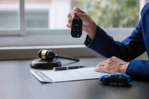 Person holding car key over legal document with gavel and toy car on desk, representing car accident legal process.