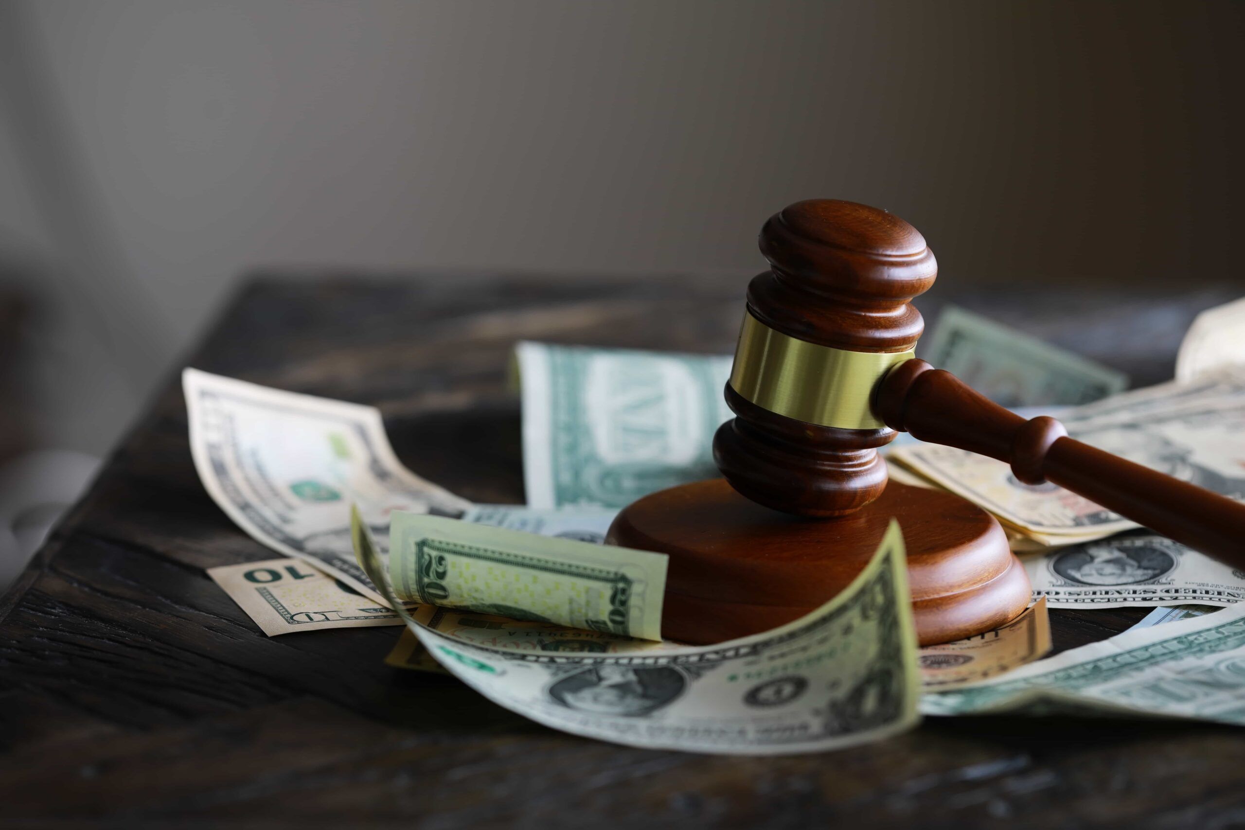 Judge&rsquo;s gavel resting on U.S. dollar bills, symbolizing legal settlements, fines, or financial compensation