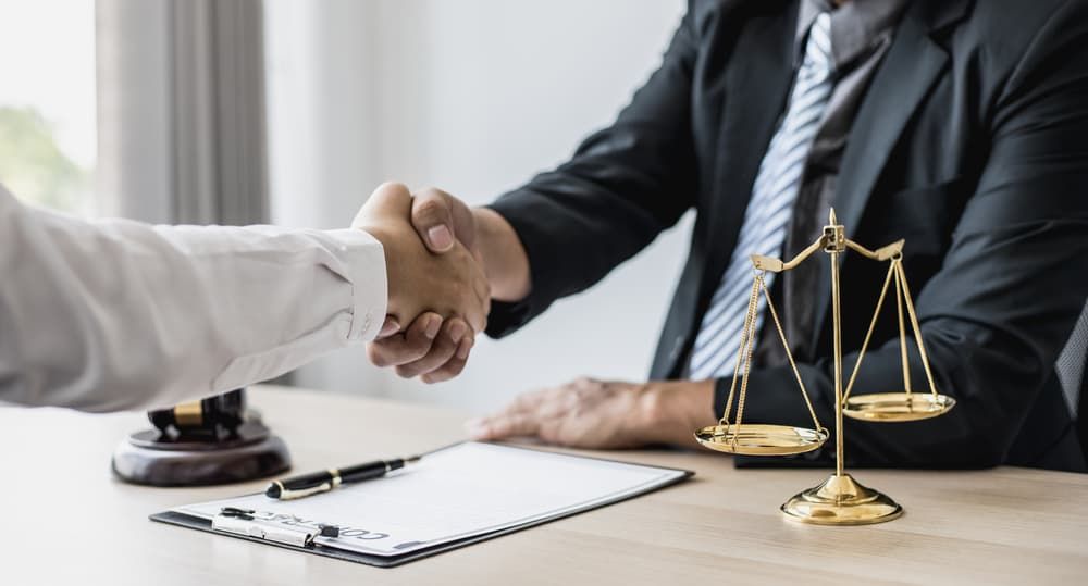Aperto de mão entre um advogado e um cliente em um ambiente formal, com uma prancheta e uma balança de justiça por perto - representando uma consulta jurídica bem-sucedida após um acidente de motocicleta.