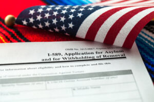 U.S. asylum application form (I-589) with an American flag draped over the corner.