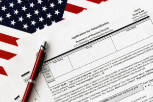 USCIS Form N-400 Application for Naturalization with a pen placed on top of the form, partially covering an American flag in the background