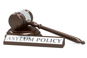 Wooden judge's gavel resting beside a nameplate reading 'Asylum Policy' symbolising legal decisions on immigration and asylum cases.