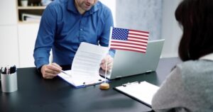 Man sitting at a desk reviewing immigration paperwork with a client, small American flag displayed on the desk, representing legal immigration services.