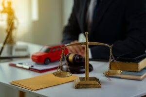 Scales of justice on lawyer’s desk with gavel, toy car, and legal documents, symbolizing car accident case.
