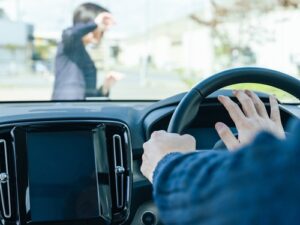 Driver pressing the horn while approaching a pedestrian crossing unexpectedly in front of the vehicle, viewed from inside the car.
