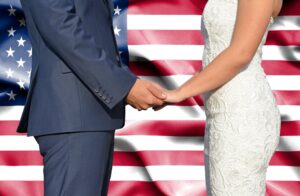 Couple in wedding attire holding hands in front of an American flag, symbolizing proving a bona fide marriage for U.S. immigration and green card process.