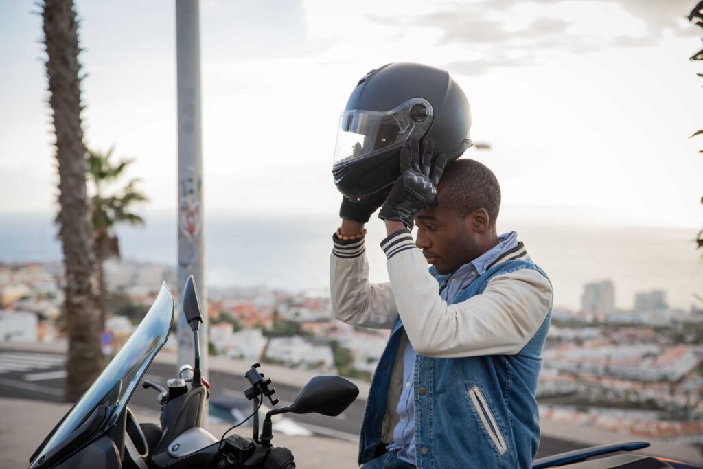 Motorcycle rider putting on helmet next to scooter overlooking city landscape.
