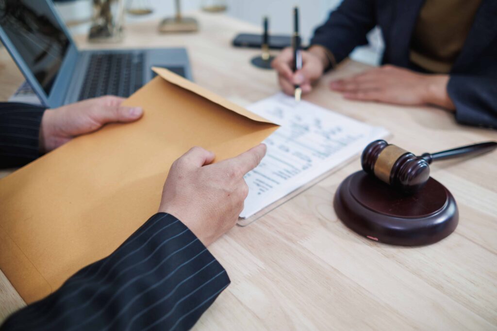 Attorney reviewing legal documents while client signs paperwork next to a judge&rsquo;s gavel.