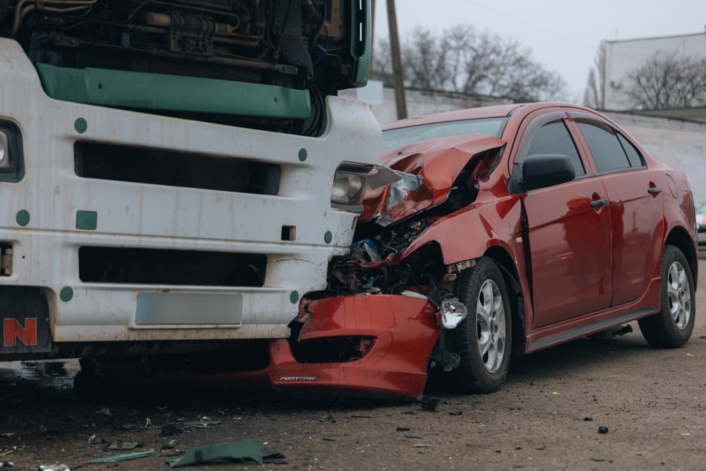 Passenger car with severe front-end damage after a collision with a large truck, illustrating the dangers and impact of truck accidents on smaller vehicles.