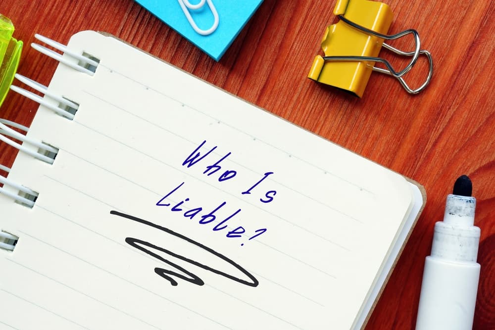 Notebook on a desk with the handwritten question &ldquo;Who is liable?&rdquo;, symbolizing responsibility and parties involved in a product liability case.