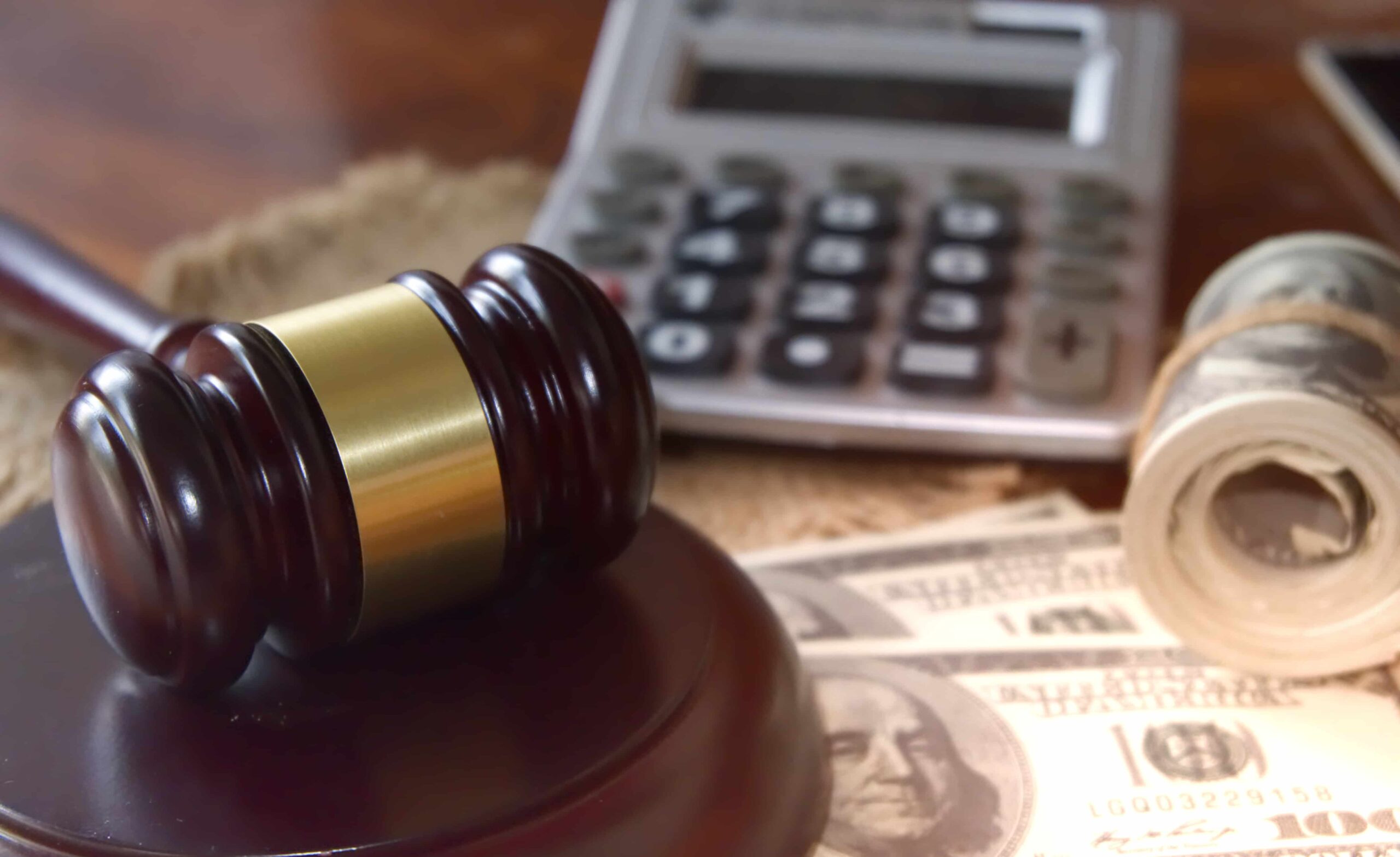 Judge’s gavel resting on U.S. dollar bills beside a calculator, symbolizing legal costs, settlements, or financial damages. Judge’s gavel resting on U.S. dollar bills beside a calculator, symbolizing legal costs, settlements, or financial damages.