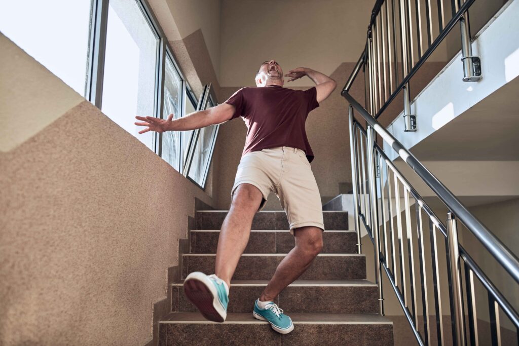 Man slipping and falling down indoor stairs, losing balance and suffering a potential stairway accident.