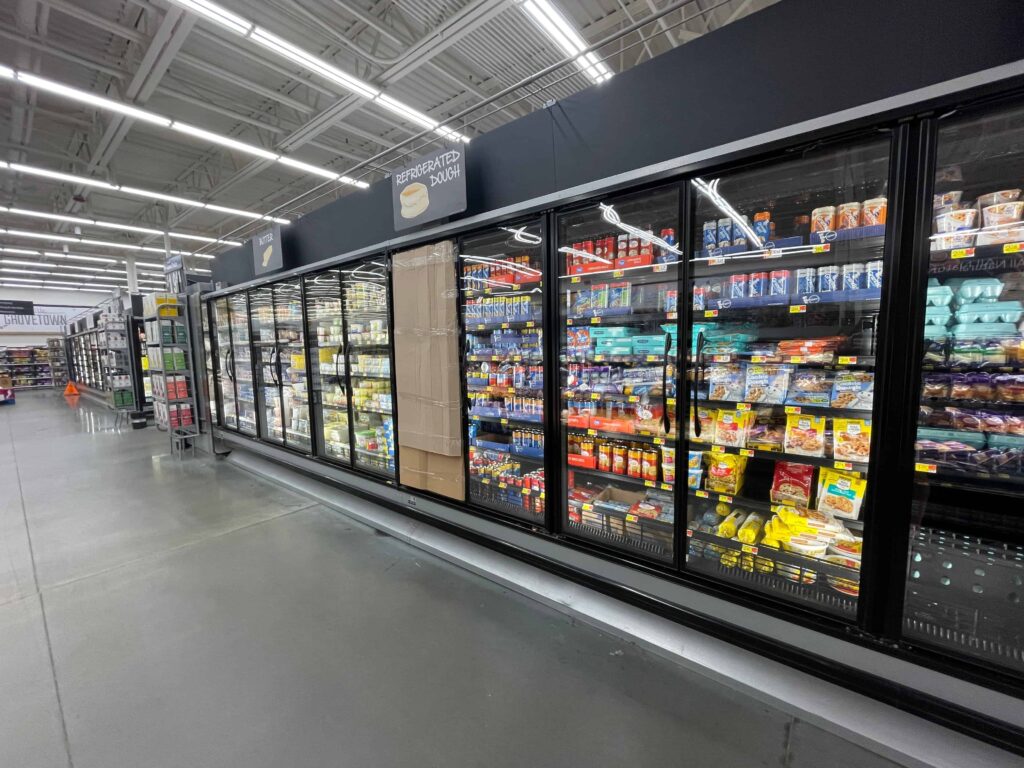 Grocery store frozen food aisle with glass-door freezers stocked with packaged foods and refrigerated products. Grocery store frozen food aisle with glass-door freezers stocked with packaged foods and refrigerated products.