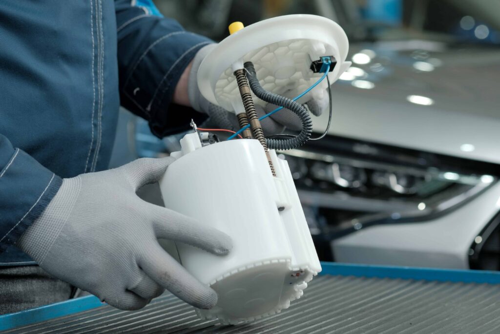 Automotive technician holding a car fuel pump assembly during vehicle repair or replacement.