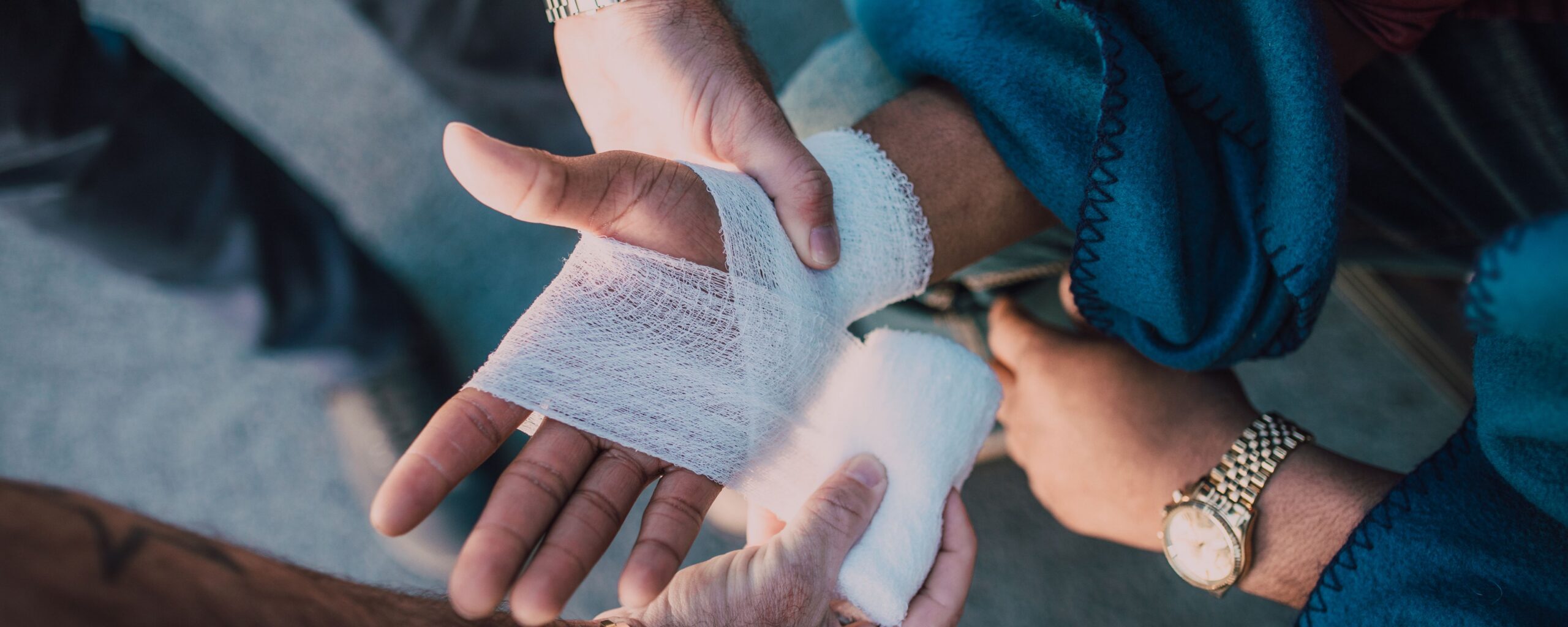 Una persona que envuelve con una venda de gasa blanca la mano y la muñeca lesionadas de otra persona